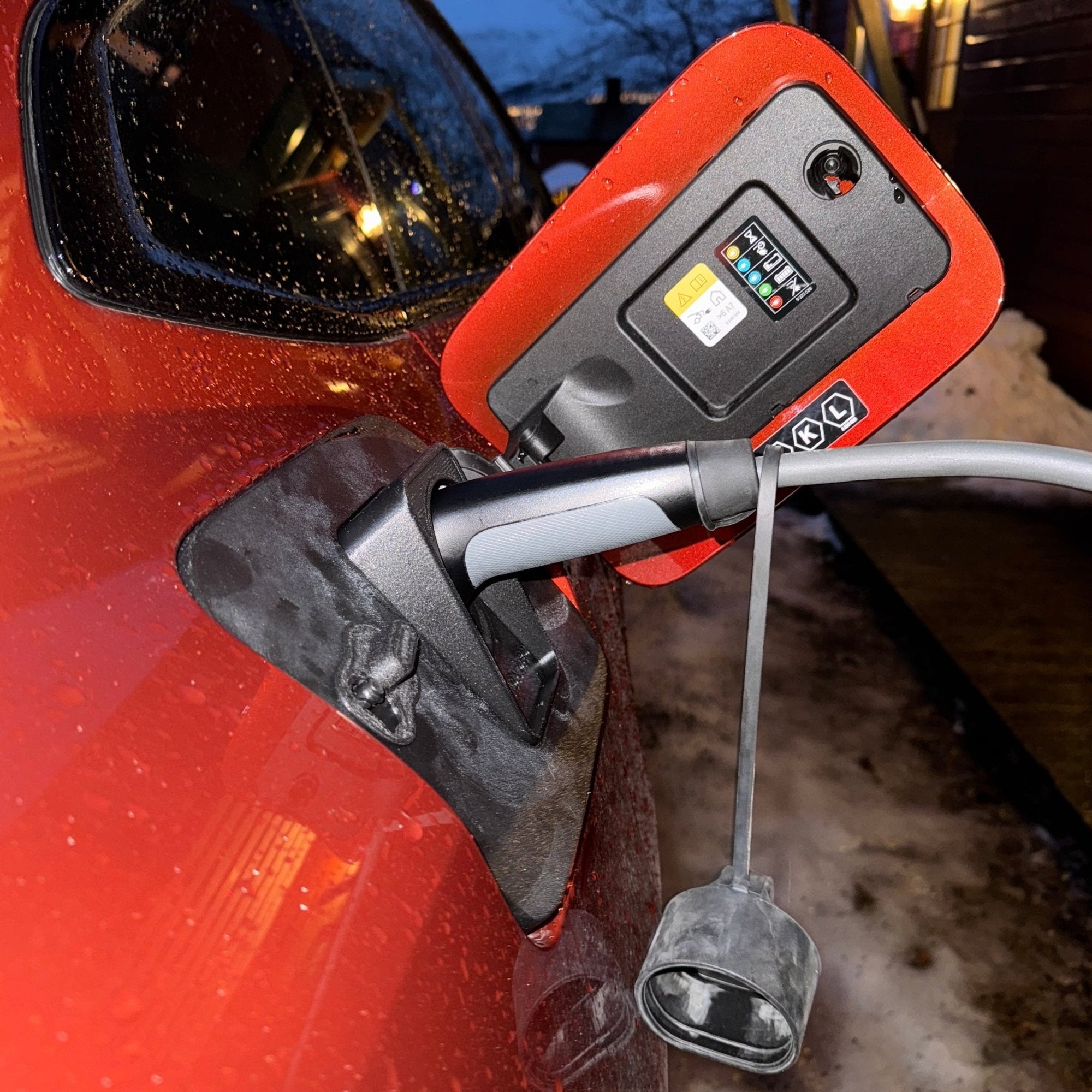 Ladestrømpe over ladekabel på rød elbil en vinterkveld